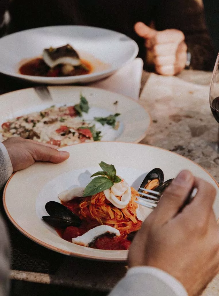 Plato de pasta fresca con mariscos, salsa de tomate y albahaca, servido en una mesa con otros platos gourmet y una copa de vino tinto